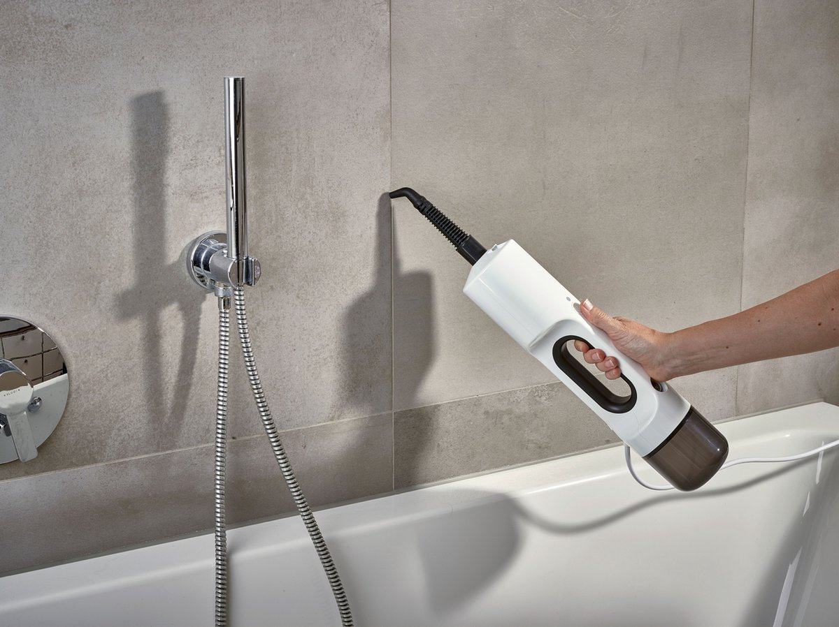 Kobieta sprząta łazienkę urządzeniem ręcznym, w tle słuchawka prysznicowa.