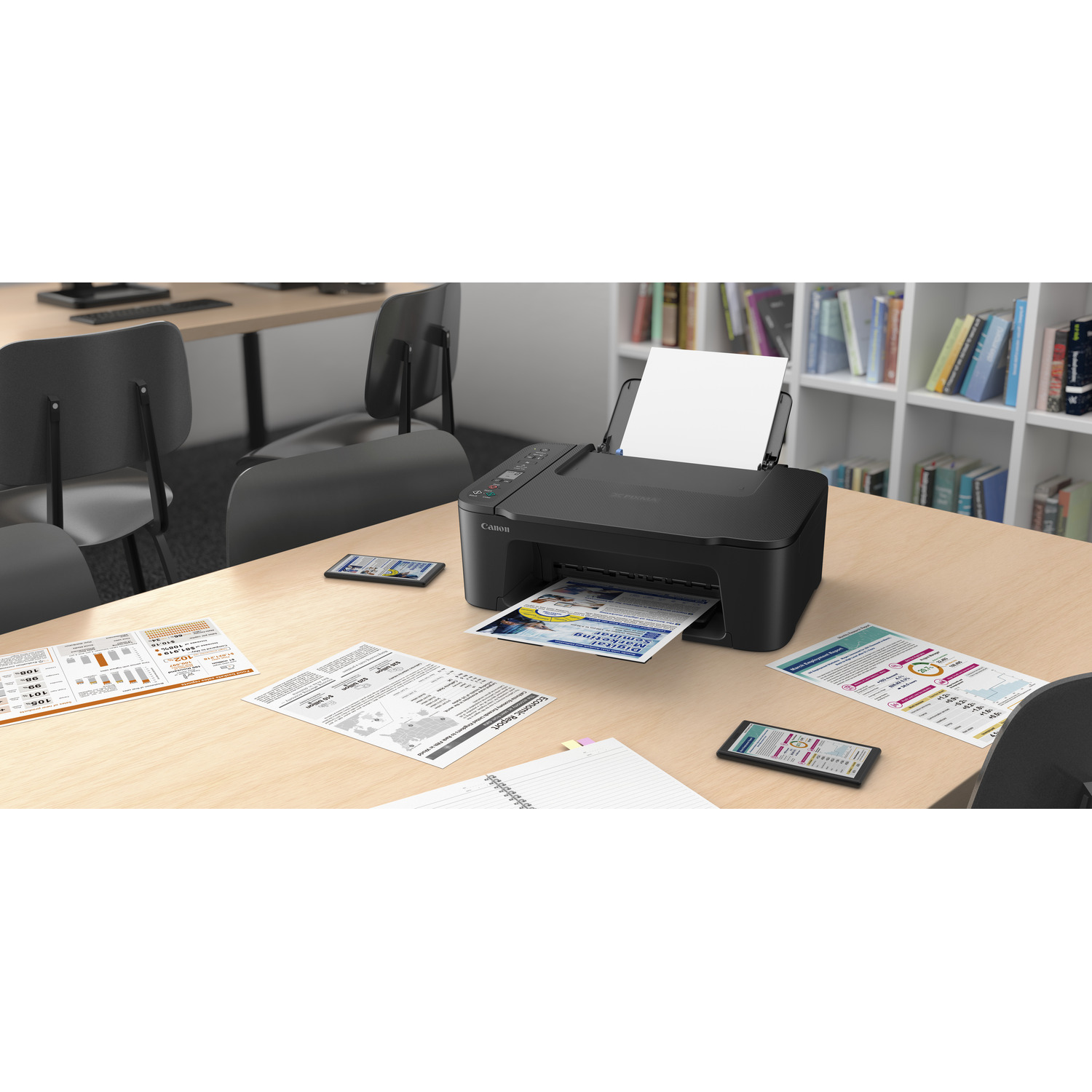 Printer on a wooden desk with papers and phones. Bookshelf with books in the background.