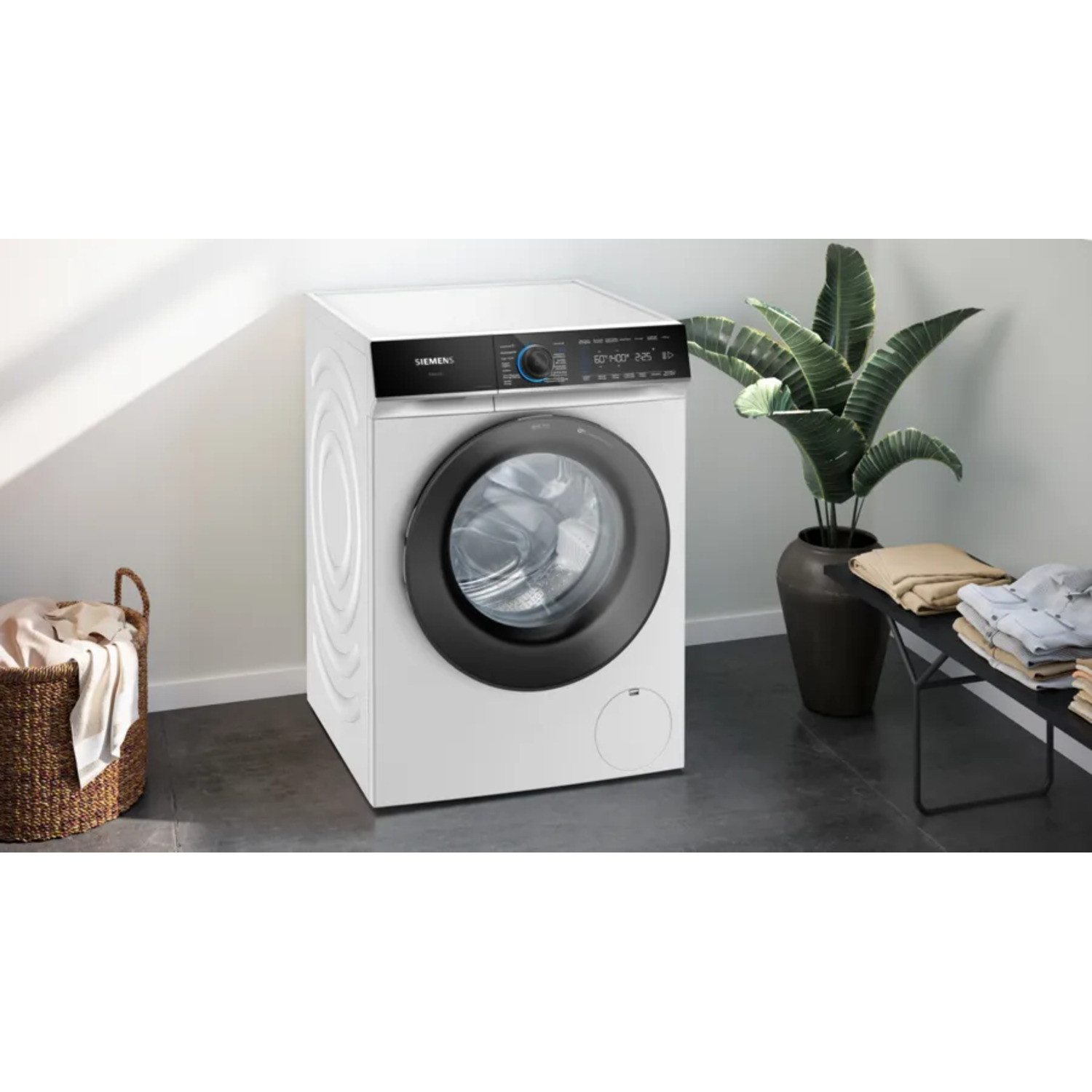 A white washing machine. It is in a room with a basket and a plant.