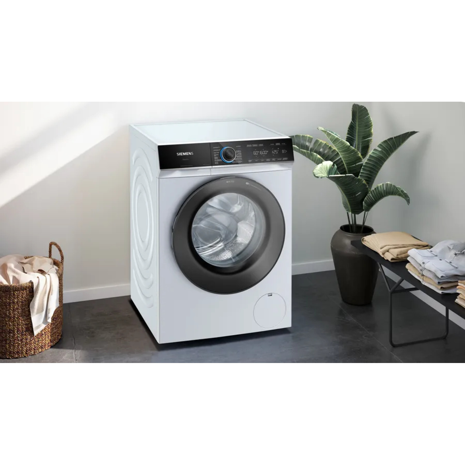 A white washing machine with a black door, next to a plant and basket.