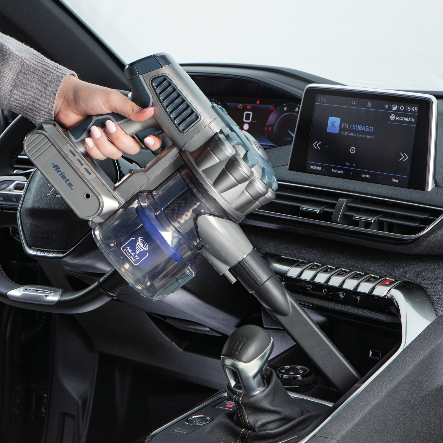 Mano che usa un aspirapolvere senza fili in auto. Cruscotto visibile. Interni auto.