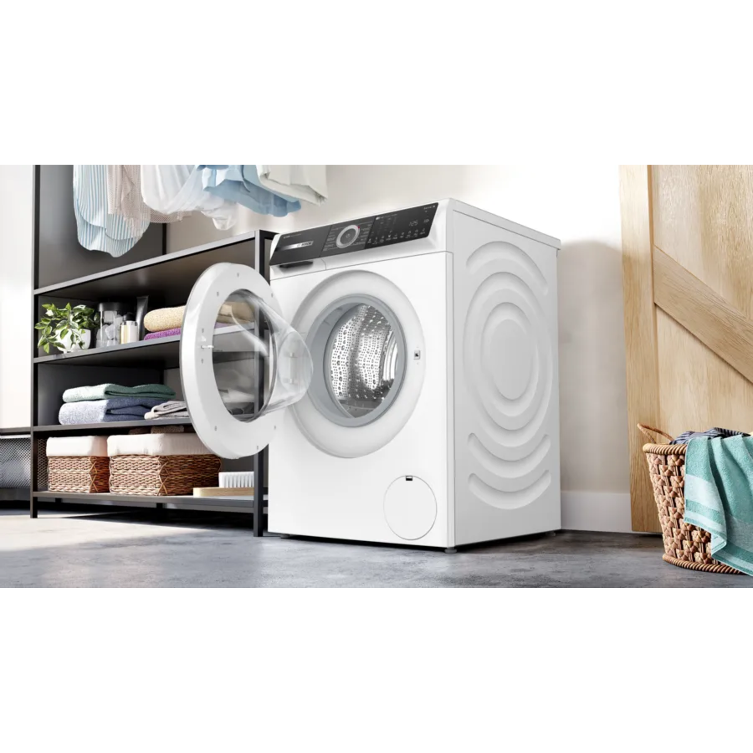 Witte wasmachine met open deur, wasgoed op de achtergrond.