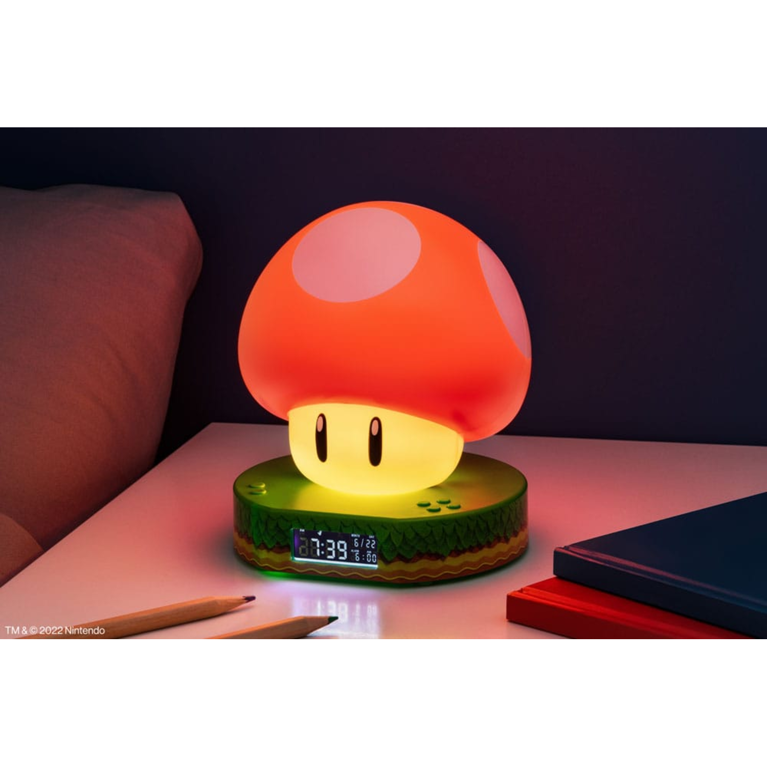 Mario mushroom lamp on a nightstand. Red top with white dots, green base, and digital clock.