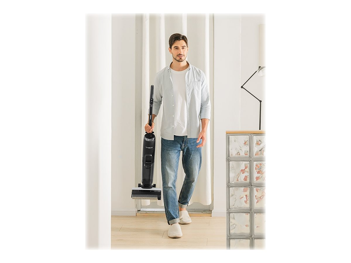 Ein Mann geht auf den Betrachter zu und hält einen schwarzen Staubsauger. Er trägt Jeans und ein helles Hemd.