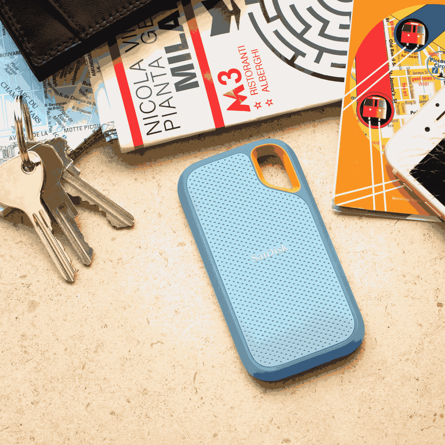Una funda de teléfono azul claro sobre una mesa, con llaves, una cartera, un mapa. La funda tiene acentos naranjas.