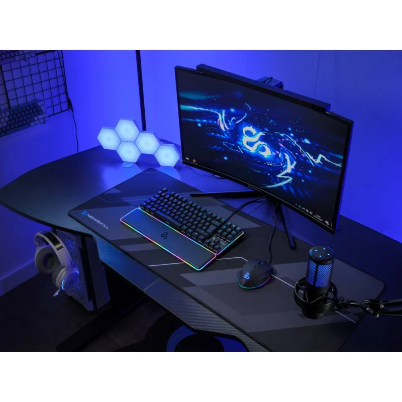 Configuración de juego con monitor, teclado, ratón, auriculares y micrófono. Luz ambiental azul.