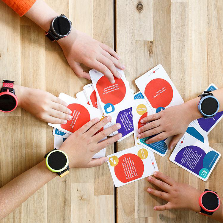 Hände, die mit Karten und Smartwatches interagieren. Karten haben Text, Uhren sind schwarz mit farbigen Bändern.
