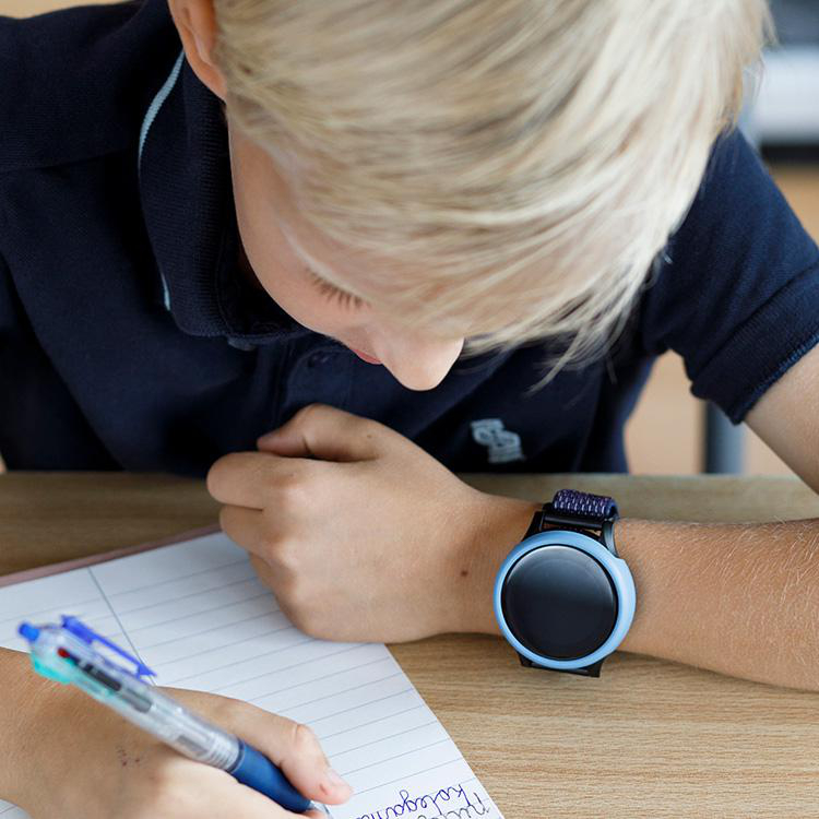 Ein Kind mit Smartwatch, schreibt in einem Notizbuch am Schreibtisch.