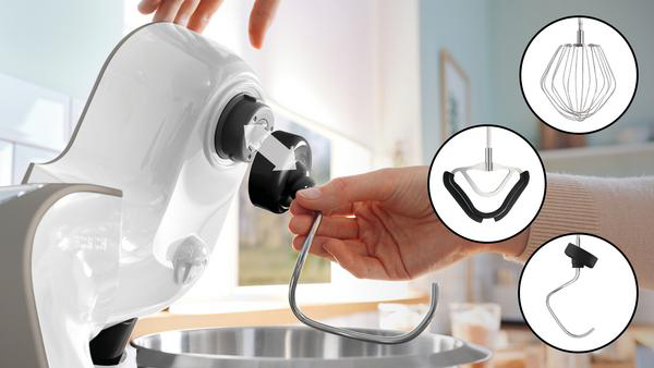 Person befestigt einen Haken an einem weißen Standmixer. Verschiedene Mixeraufsätze liegen daneben.