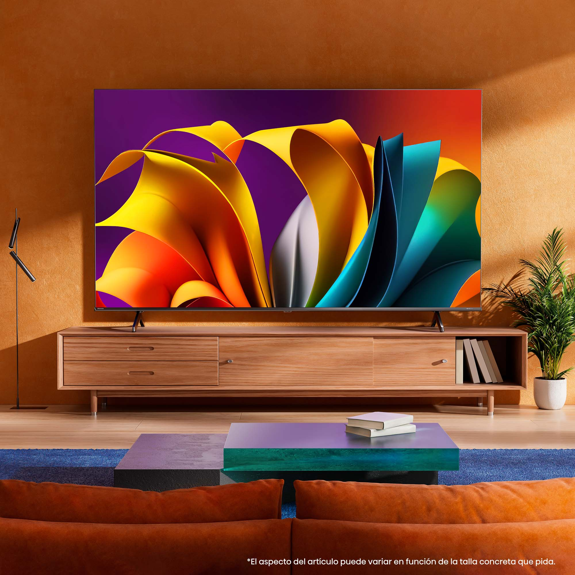 Un televisor grande muestra una imagen colorida. Está sobre un mueble de madera con una alfombra azul y pared naranja.