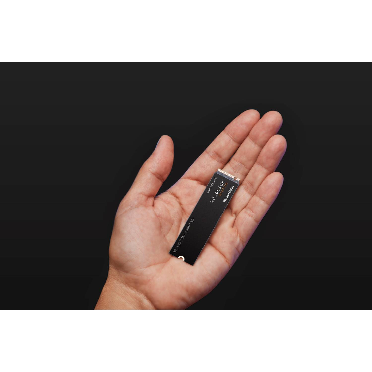 Una mano sosteniendo una SSD WD_BLACK negra sobre un fondo oscuro.