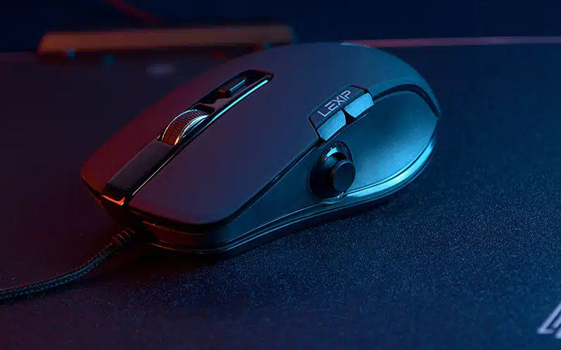 Dłoń trzymająca czarny cylindryczny głośnik z pomarańczowym paskiem, na białym tle.