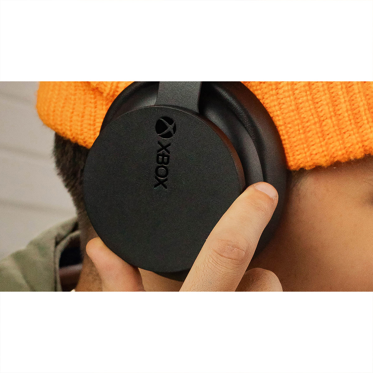 Una persona con un gorro naranja sostiene unos auriculares Xbox negros. El logo de Xbox es visible.