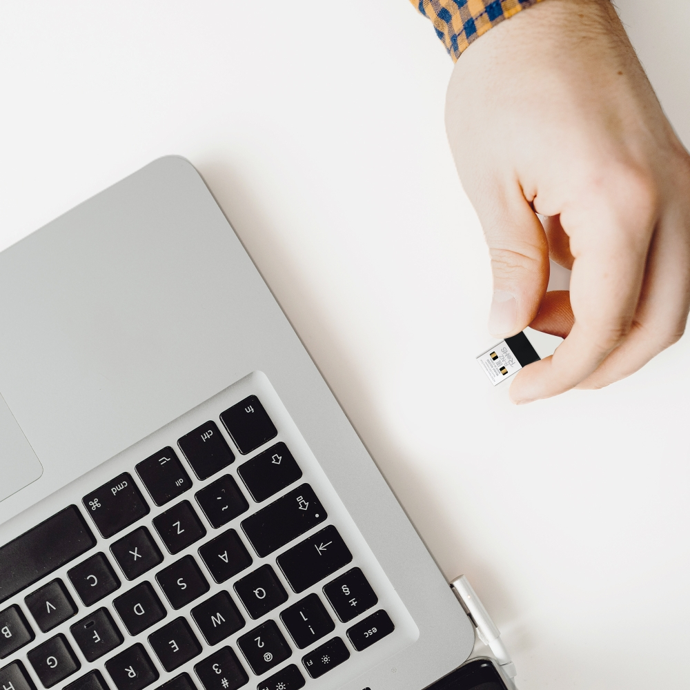 Ręka wkładająca pendrive do laptopa. Laptop i pendrive na białej powierzchni.