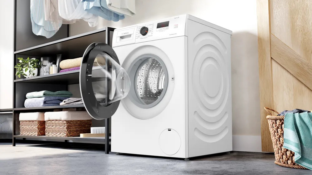 Biała pralka, otwarte drzwi pokazujące bęben, w pomieszczeniu pralni.