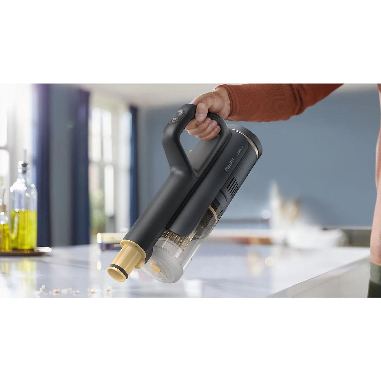 A person's hand holding a black and gold handheld vacuum cleaner on a marble surface.
