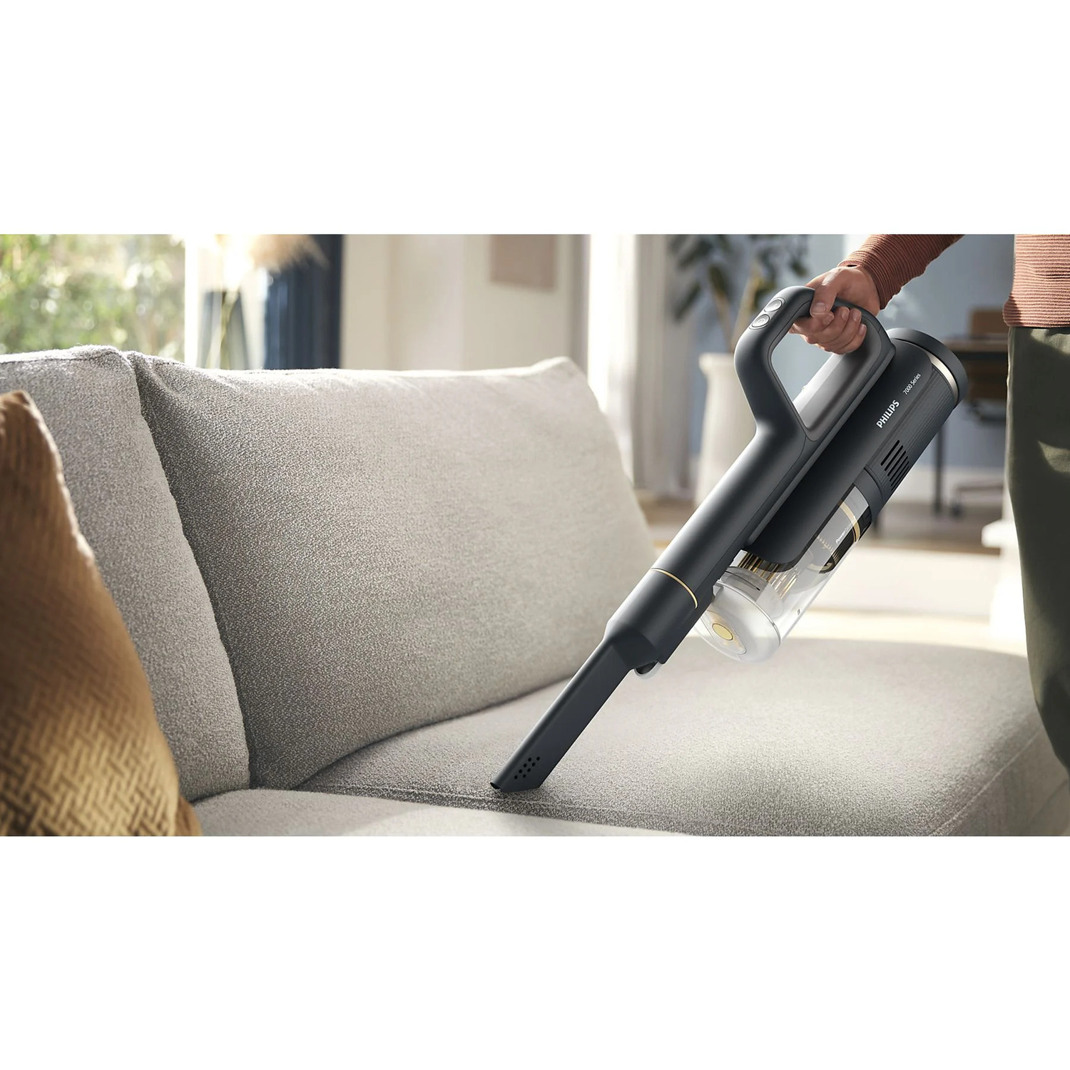 A person using a black and gold vacuum cleaner on a gray sofa.
