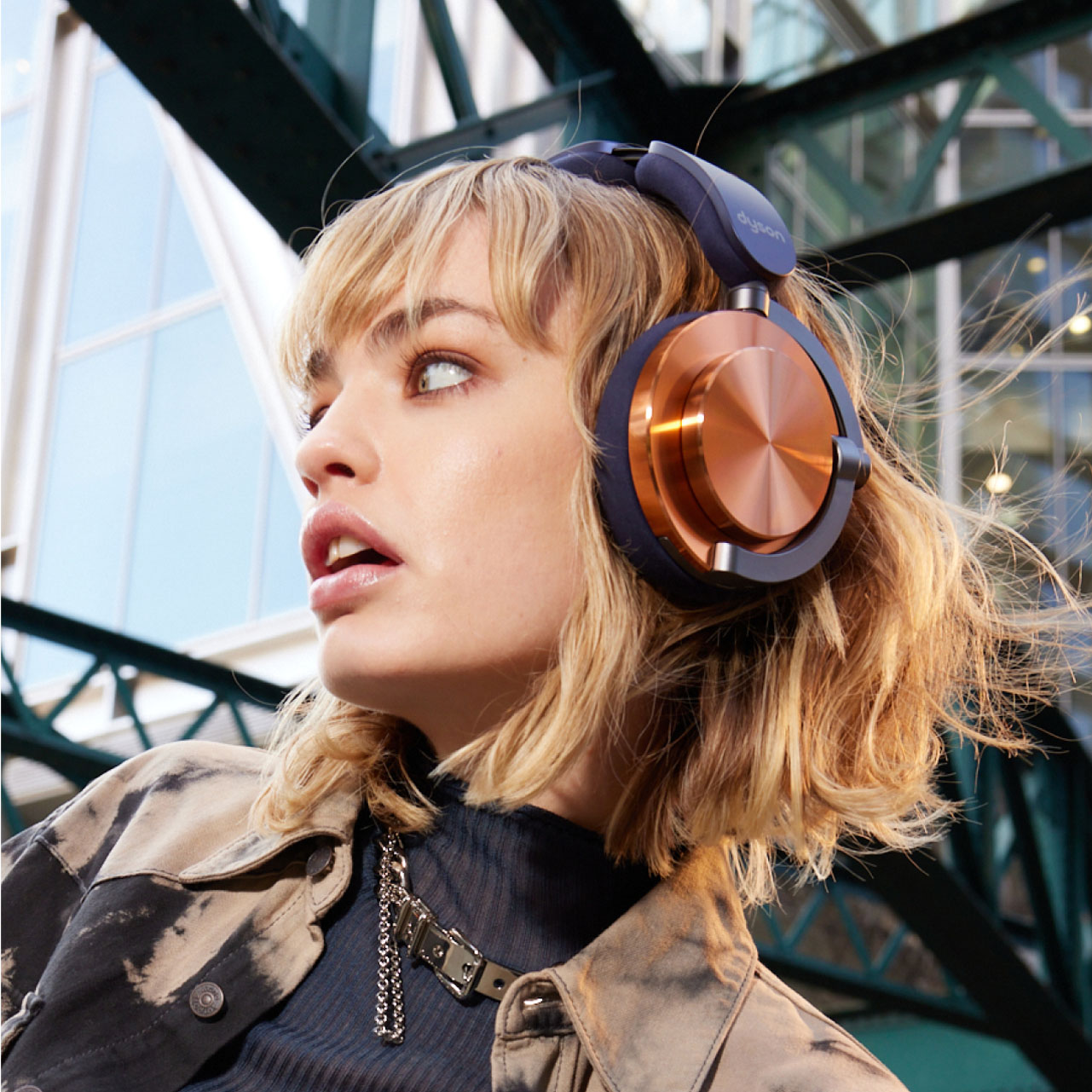 Mujer con cabello rubio usando auriculares Dyson, mirando hacia un lado.