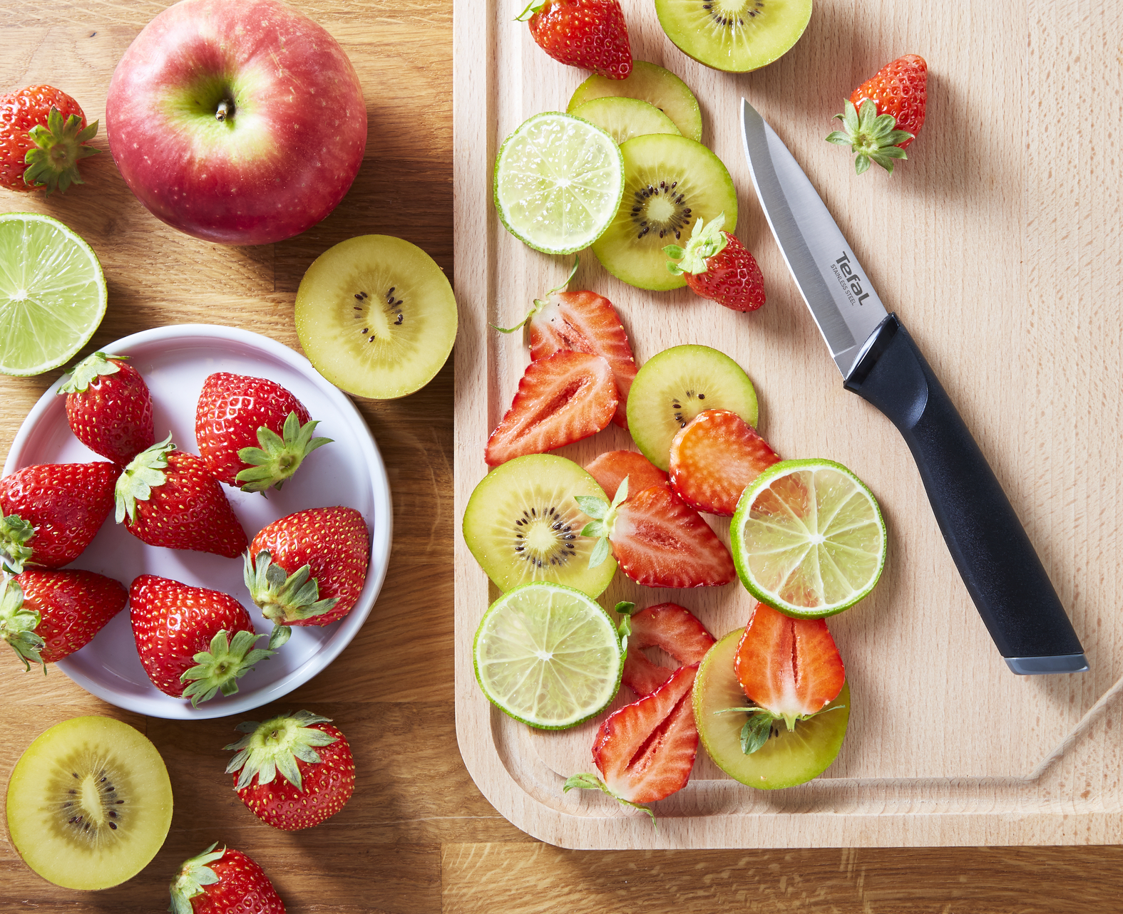 Frutas en rodajas y cuchillo sobre una tabla de madera. Fresas, kiwi, lima y una manzana.