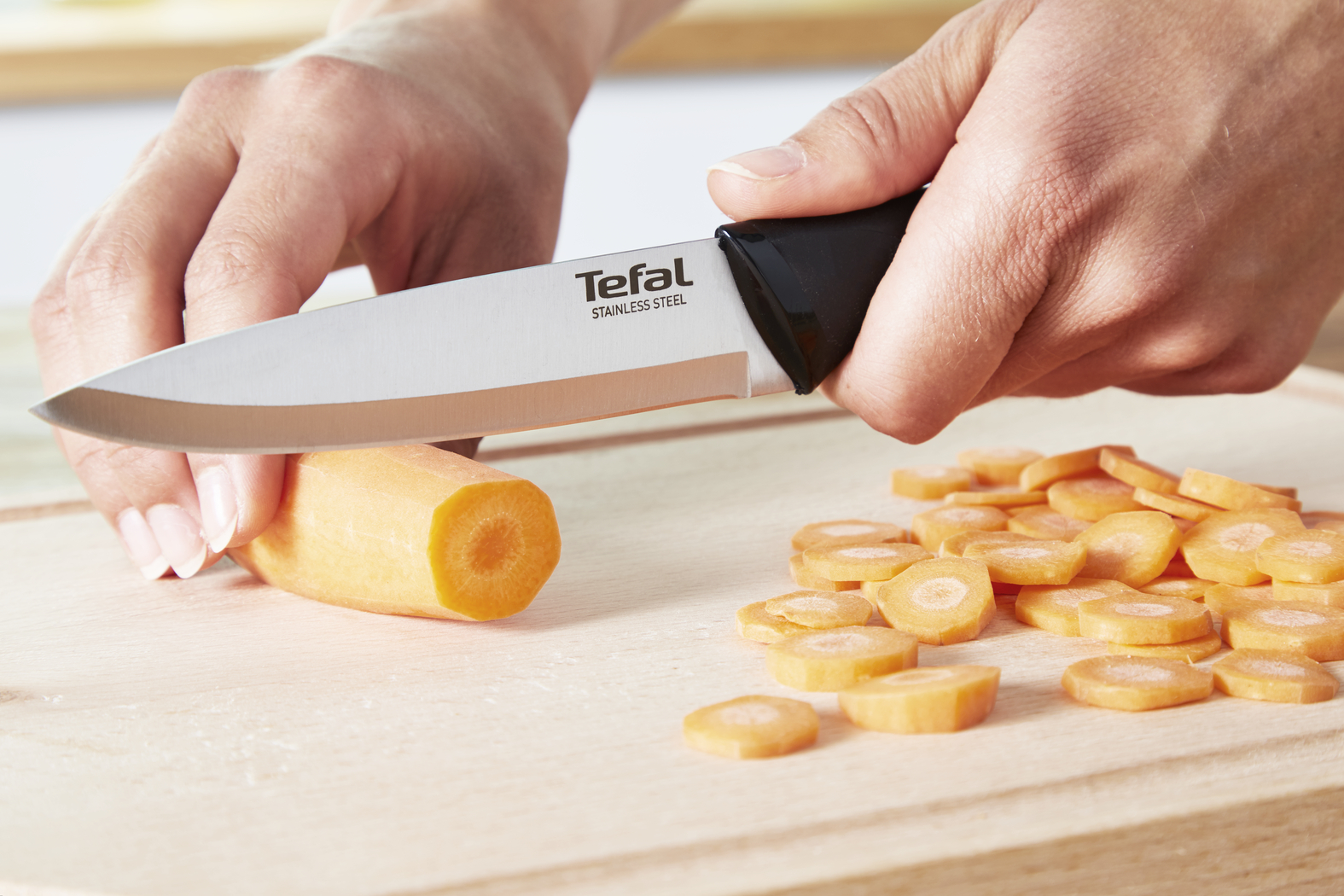 Una persona corta una zanahoria con un cuchillo TEFAL en una tabla de cortar de madera.