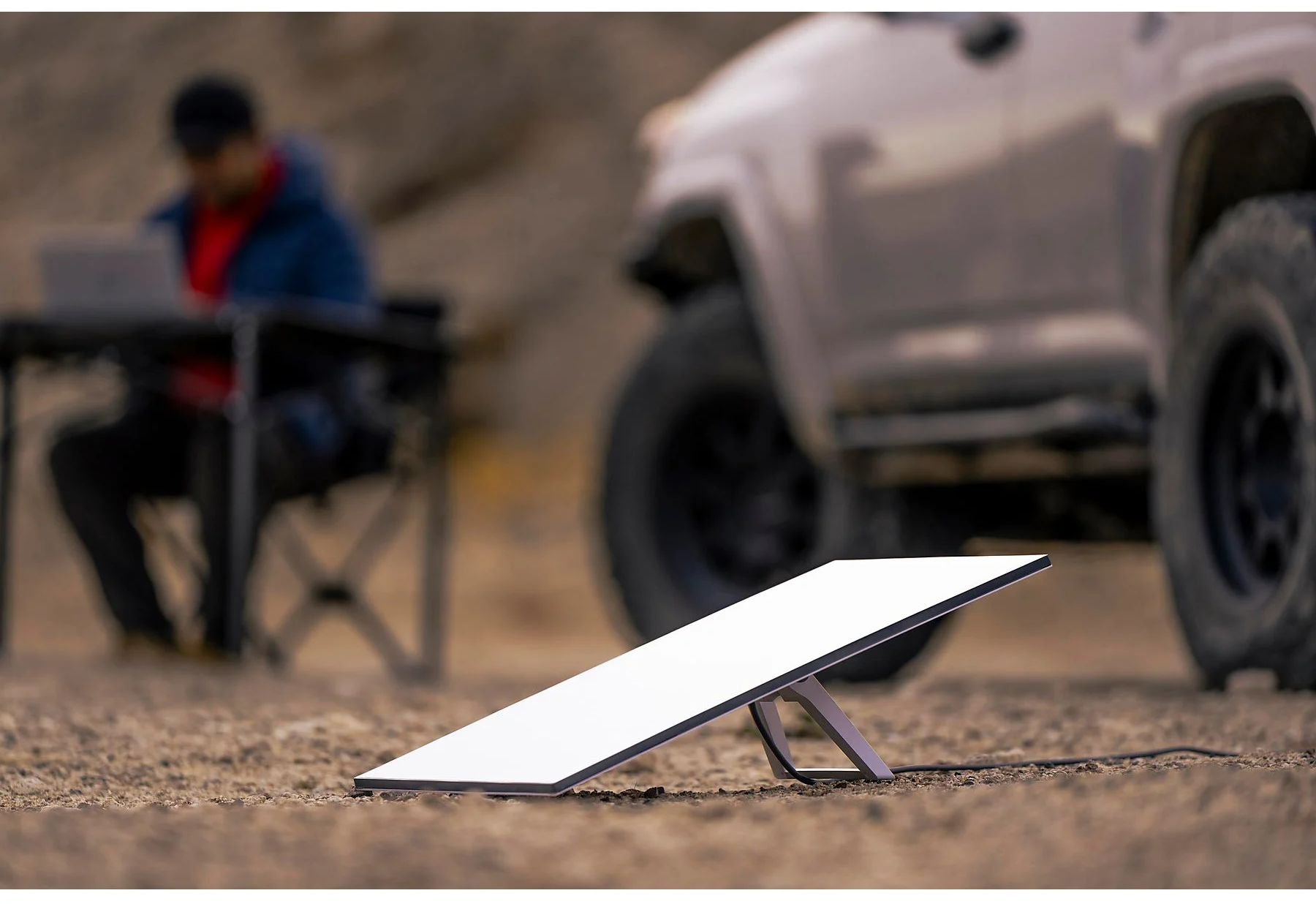 Antenna Internet satellitare angolata a terra. Persona che lavora su laptop sullo sfondo vicino a un camion.