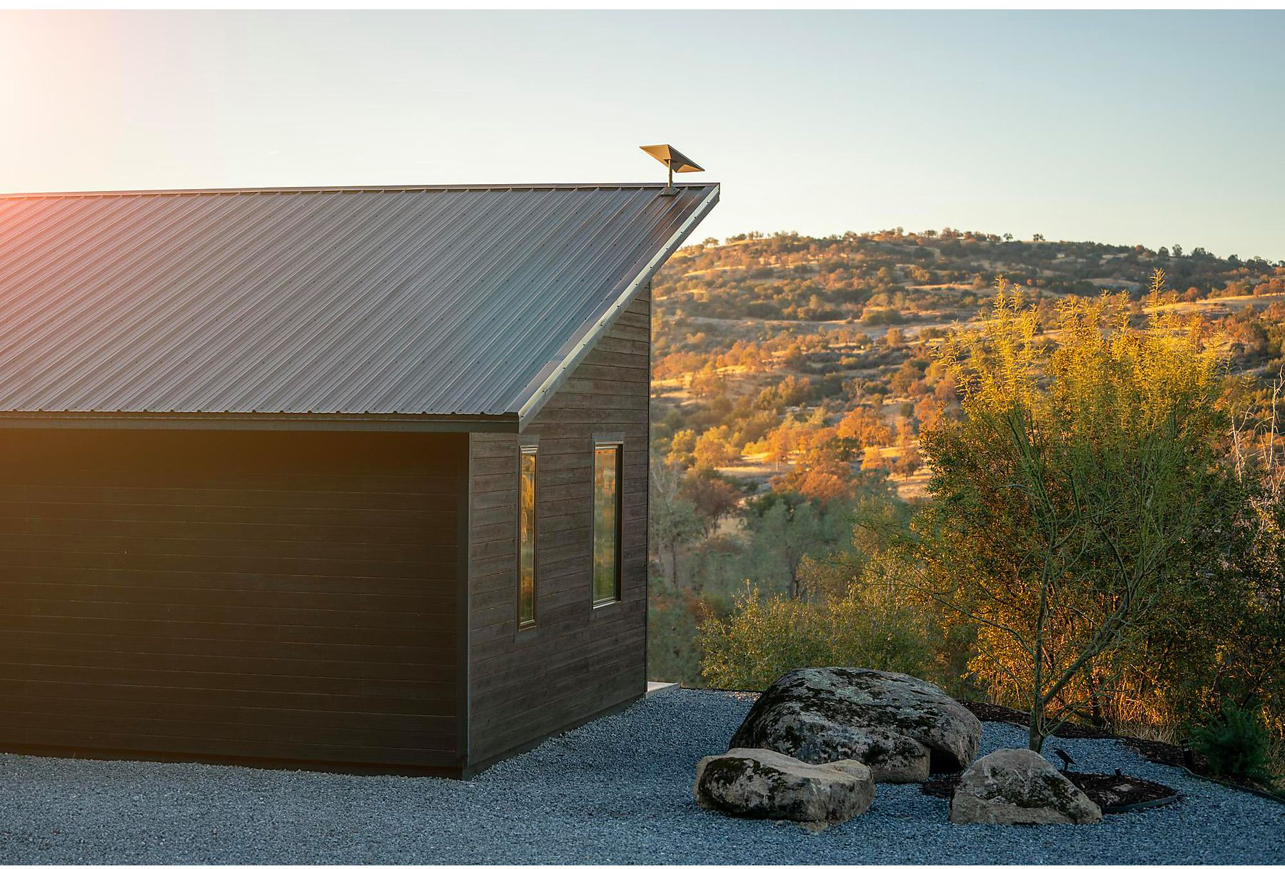 Una casa scura con un tetto in metallo e un pannello solare. Lo sfondo è un paesaggio.