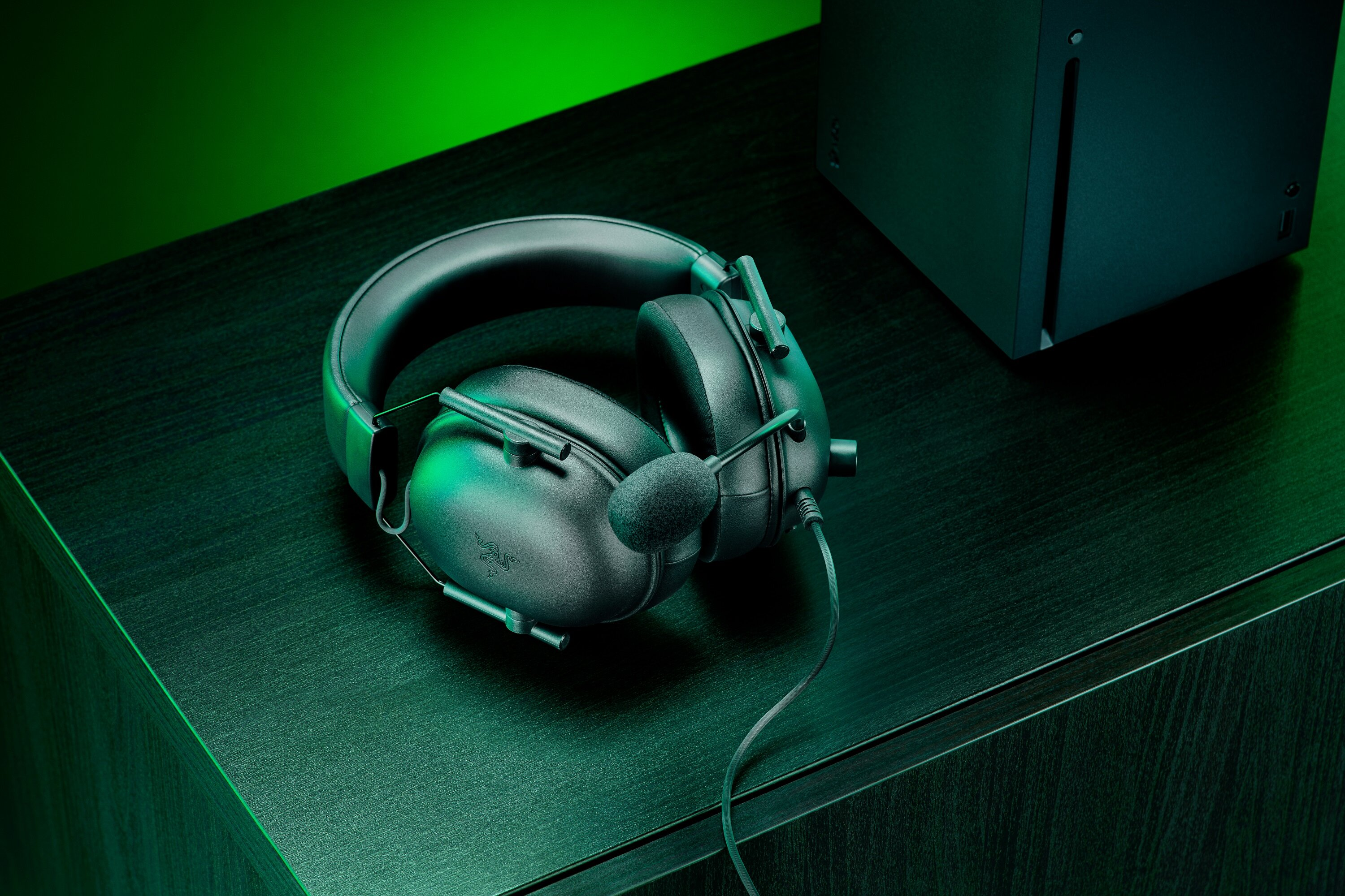Czarne słuchawki do gier na czarnej powierzchni. Zielone tło. Konsola Xbox Series X w tle.