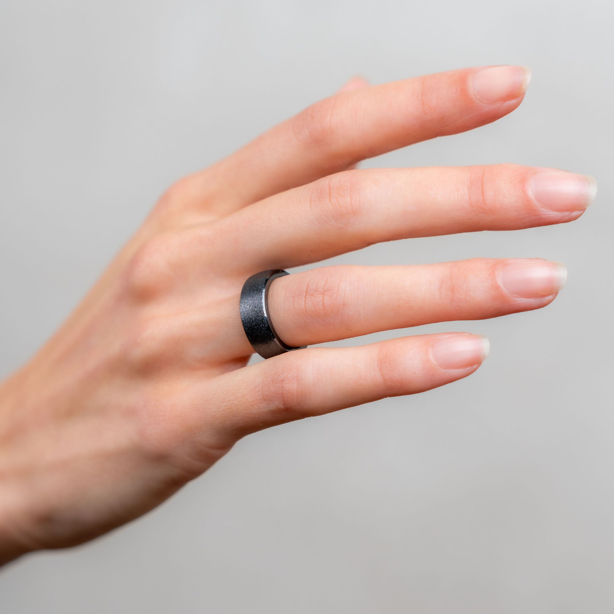 Nahaufnahme einer Hand, die einen dunklen, strukturierten Ring am Ringfinger trägt.