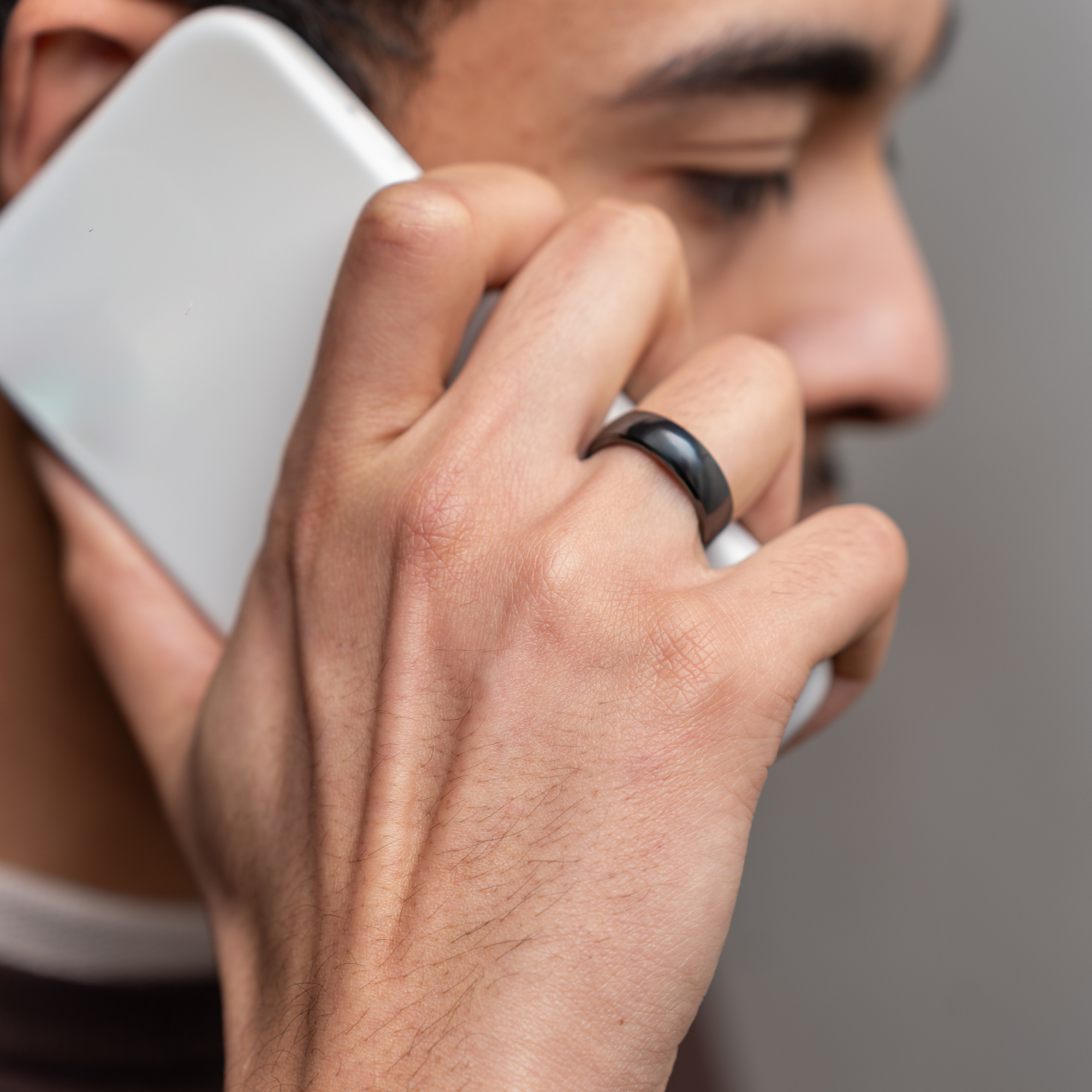 Eine Person, die ein weißes Telefon an ihr Ohr hält, trägt einen schwarzen Smartring.