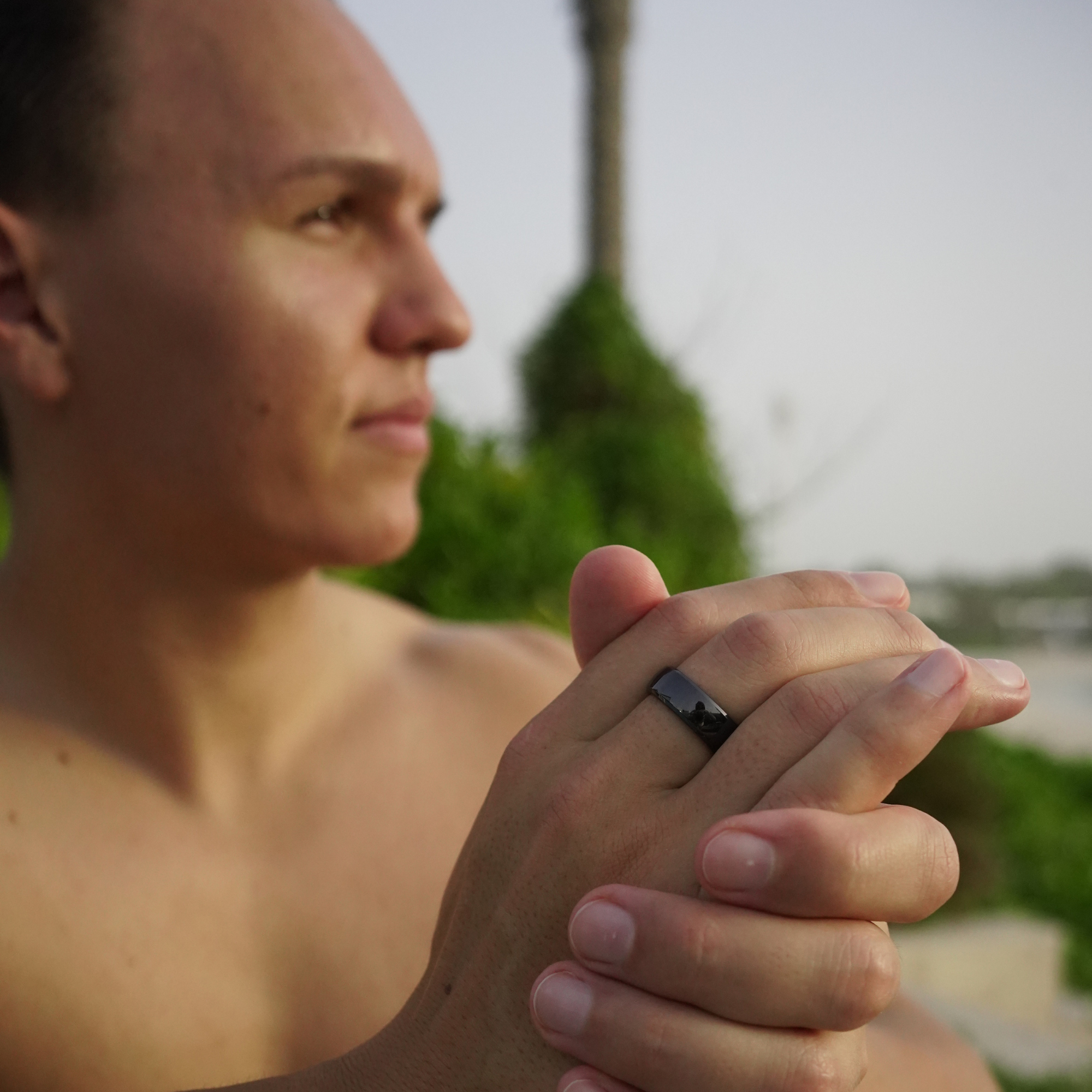 Mann mit schwarzem Ring am Finger, draußen. Weicher Hintergrund mit Grün.