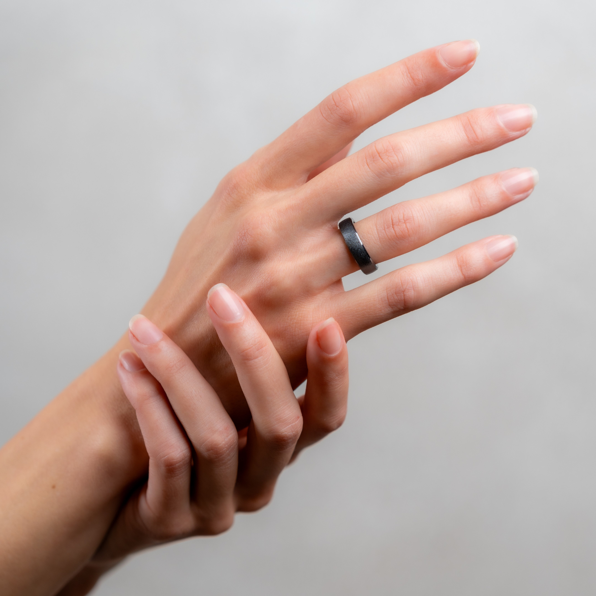 Frauenhand mit schwarzem Ring am Finger, vor hellem Hintergrund.
