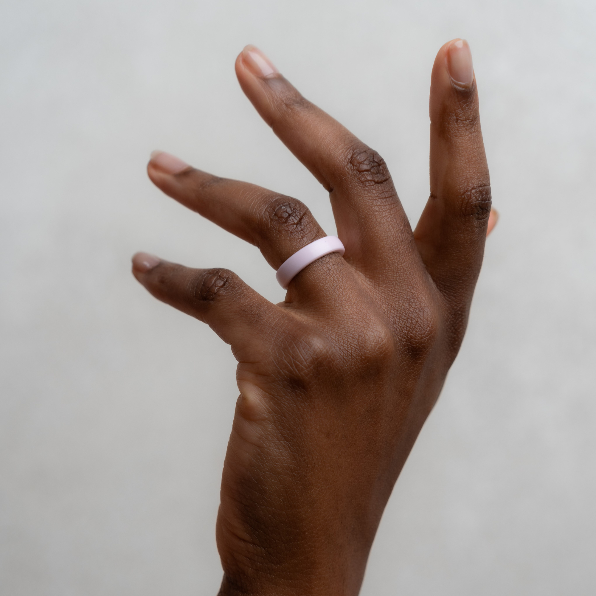 Eine Hand mit einem hellrosa Ring auf weißem Hintergrund.