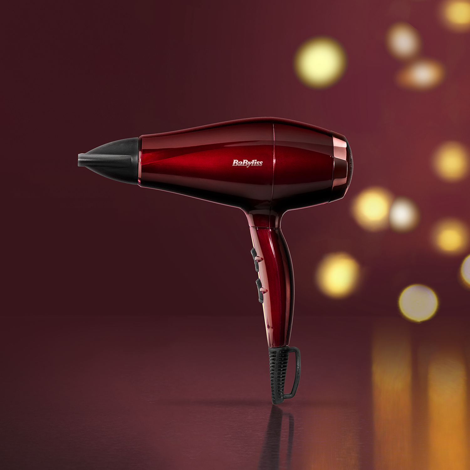 Red Babyliss hair dryer. The focus is on the hair dryer against a blurred background with bokeh lights.