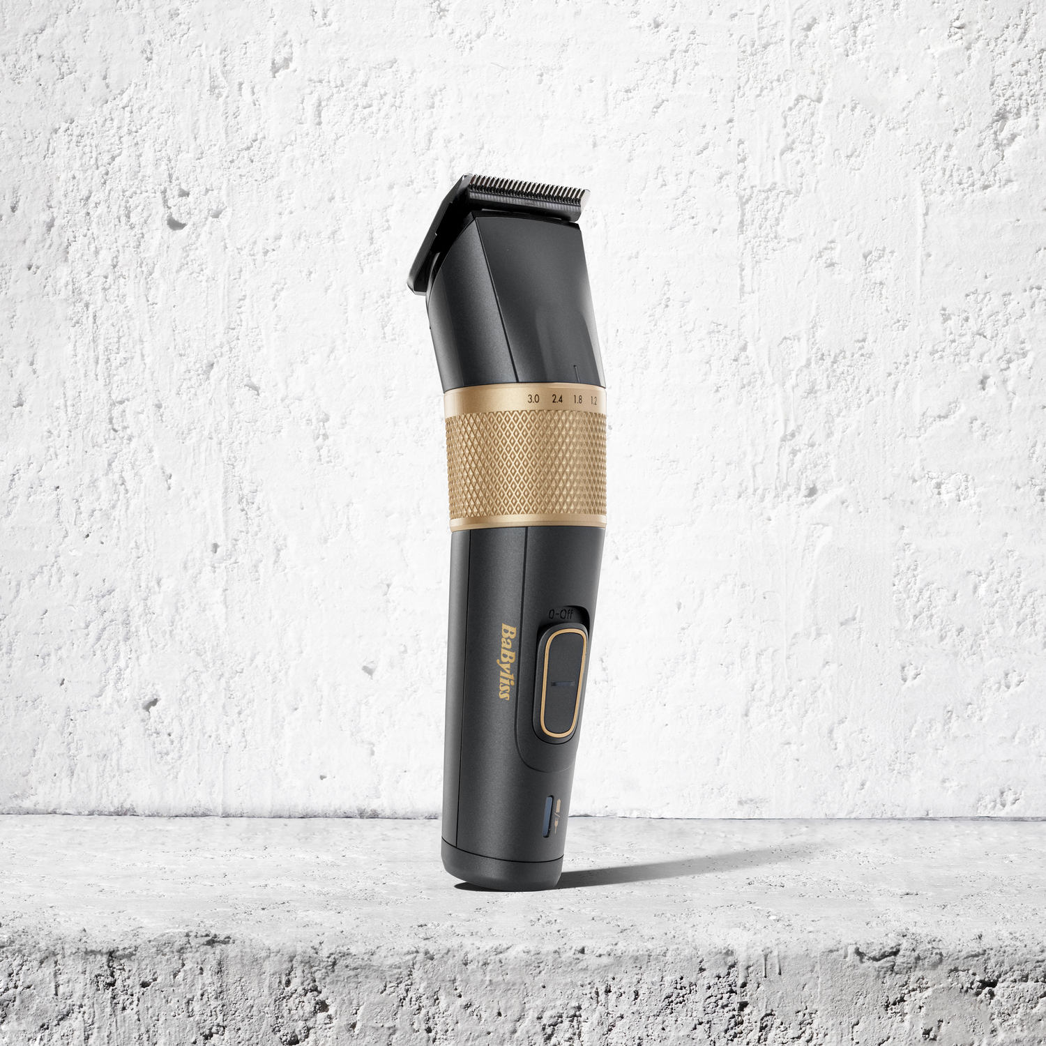 Black and gold Babyliss hair clipper on a concrete surface, against a textured white wall.