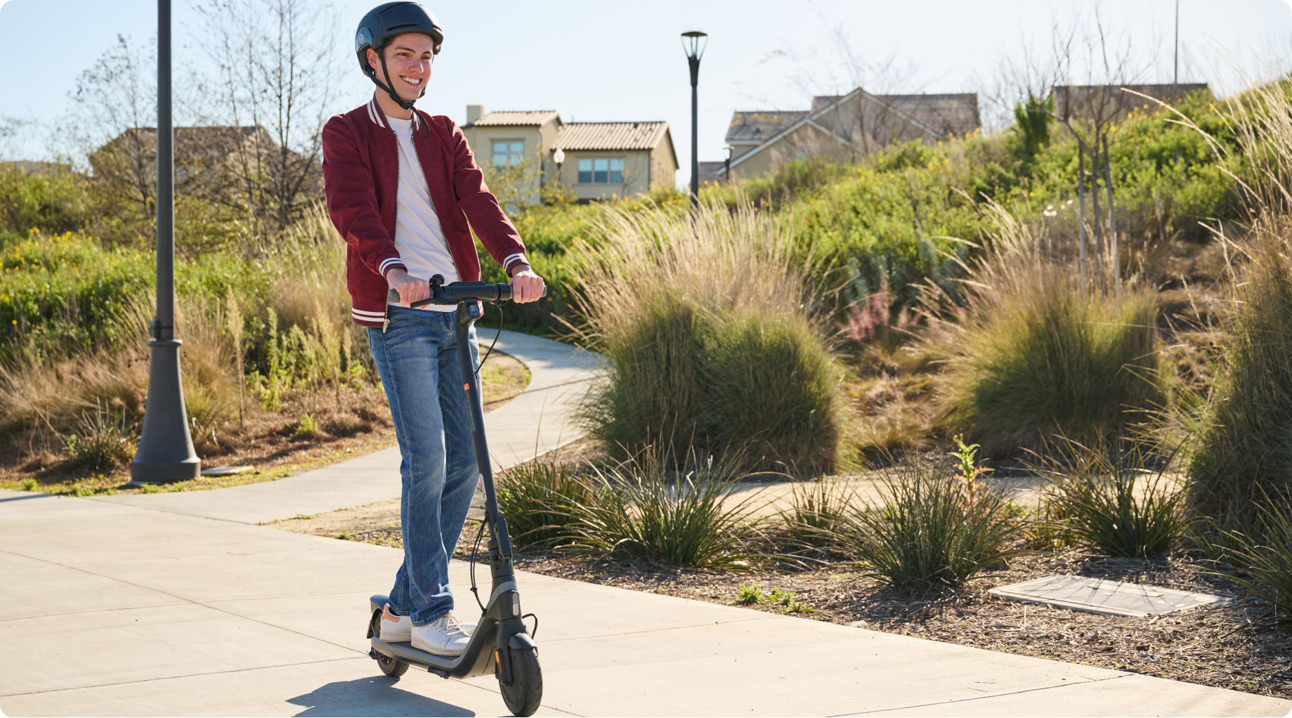 Nastolatek w kasku jeżdżący na hulajnodze elektrycznej po utwardzonej ścieżce.