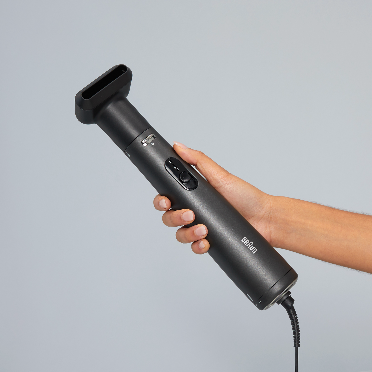 A person's hand holding a black Braun hair styling tool, pointed towards the right.