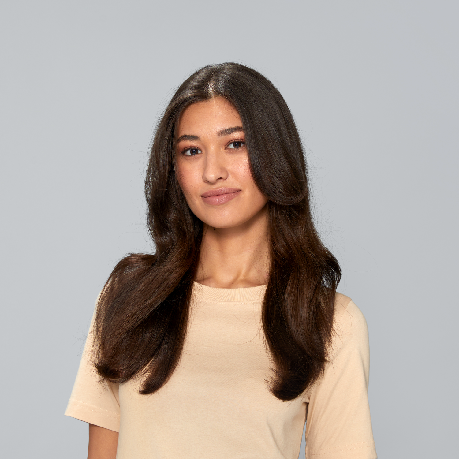 A woman with brown hair and a beige shirt smiles at the camera. The background is a soft gray.