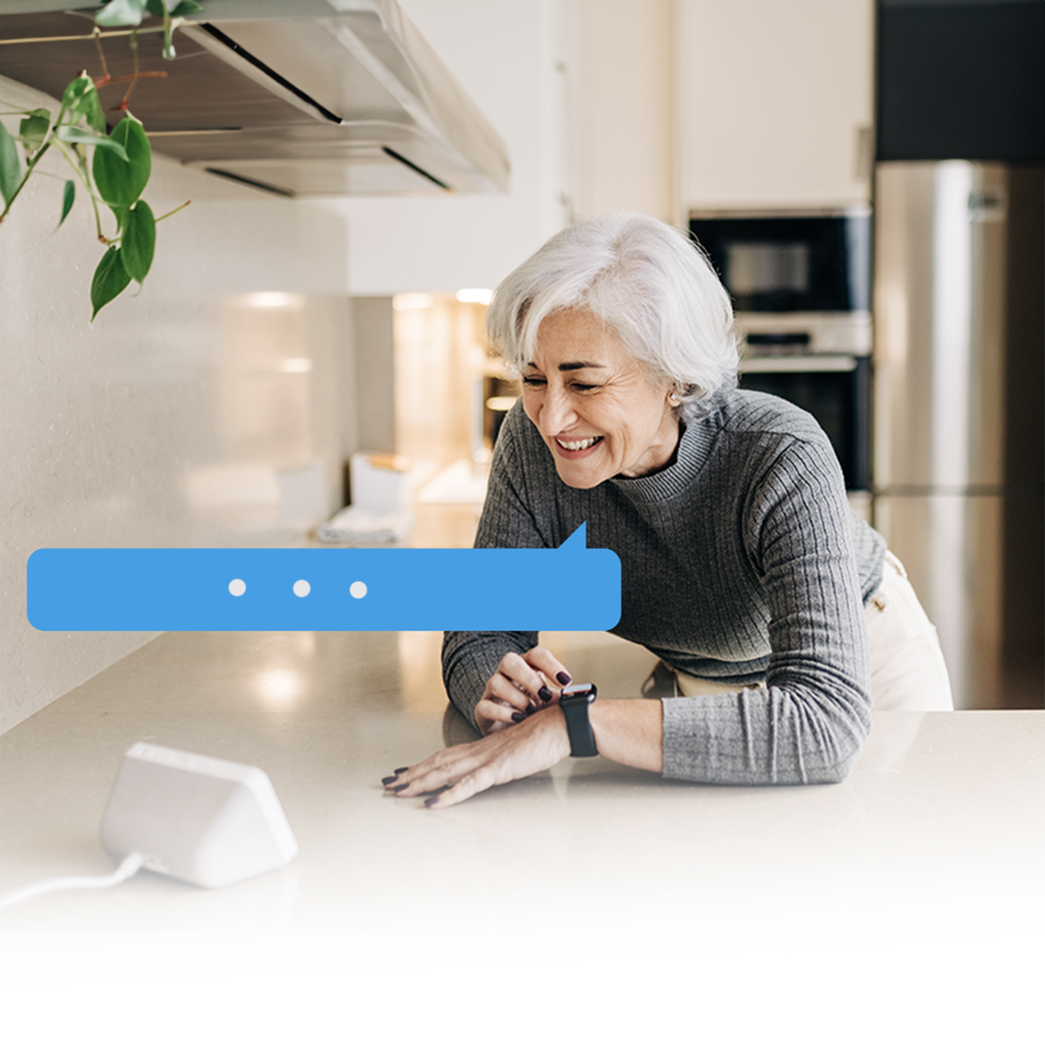 Oudere vrouw glimlacht terwijl ze kijkt naar een smart home-apparaat op het aanrecht; denkballon aanwezig.