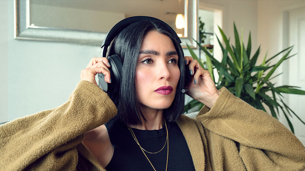 Femme portant un casque noir, l'ajustant des deux mains, assise sur un canapé.