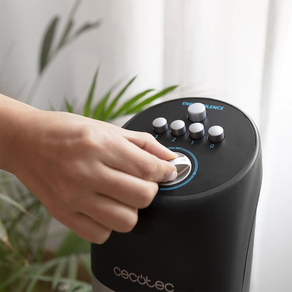 Una mano girando la perilla de un ventilador negro y gris, con botones etiquetados como 'Energy' y 'Silence'.