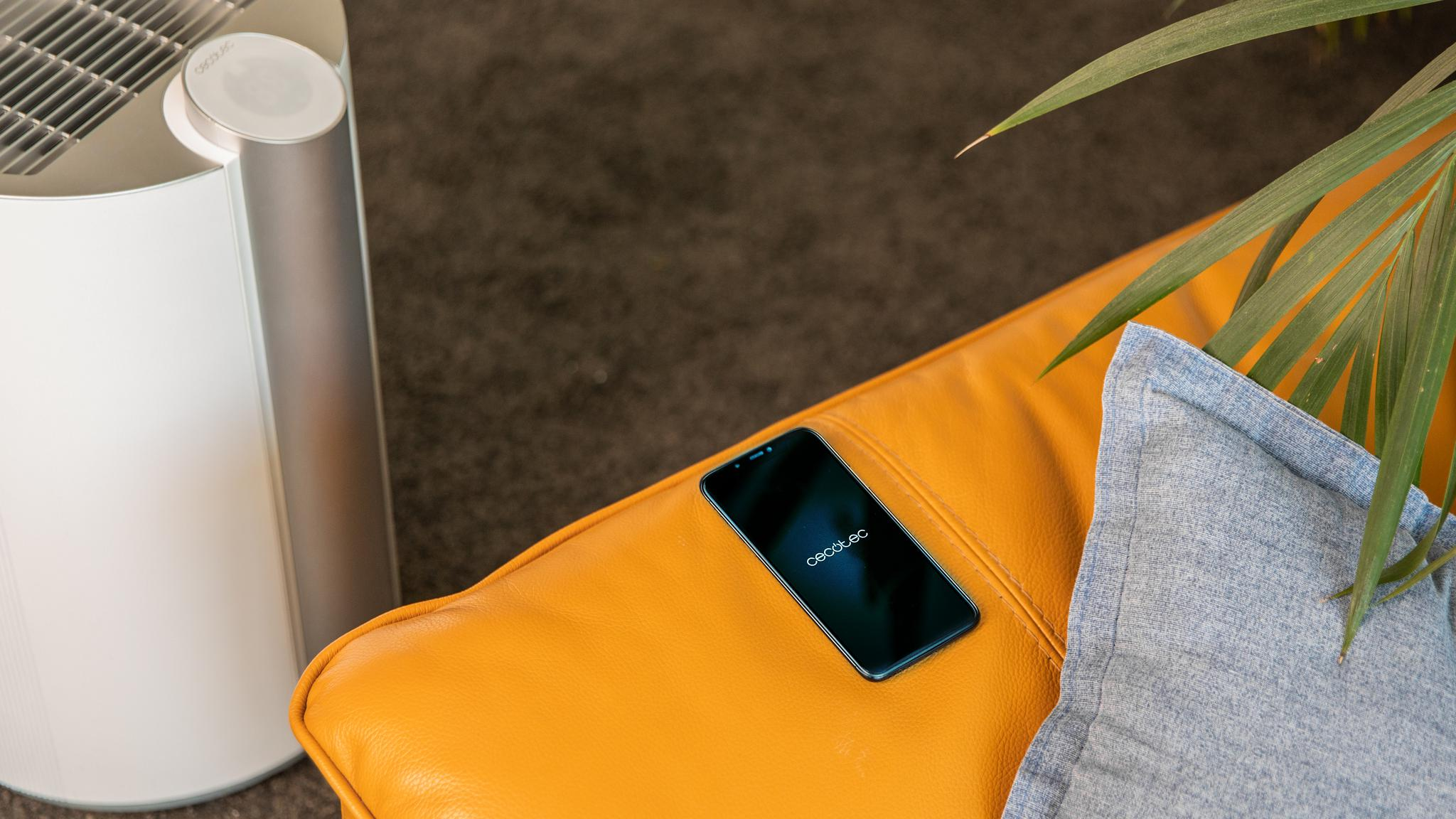 Sofá amarillo con teléfono, purificador de aire y almohada. Suelo marrón oscuro.
