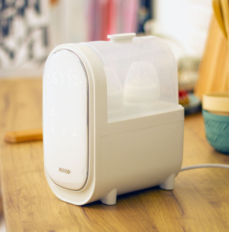 Biały sterylizator do butelek dla niemowląt z butelkami w środku, na drewnianym stole.