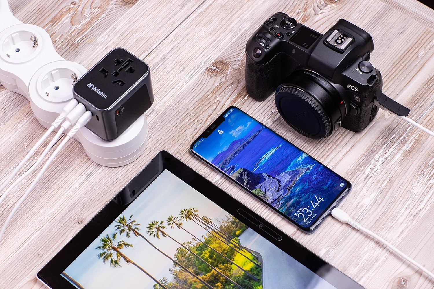 Utazó adapter, kamera, telefon és tablet, mindegyik töltődik egy fa felületen.