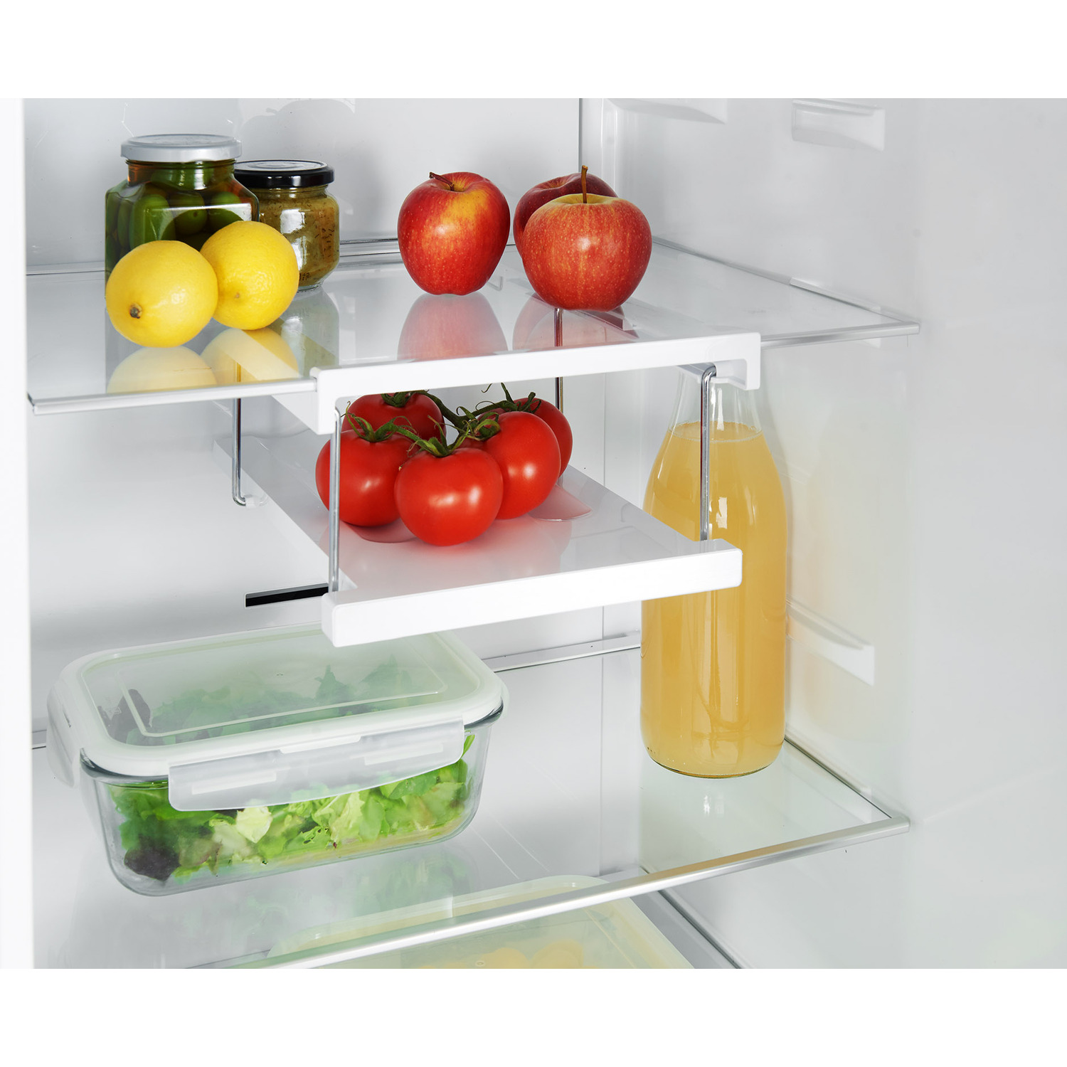 Intérieur de réfrigérateur : bocaux, pommes, tomates, bouteille de jus et salade.