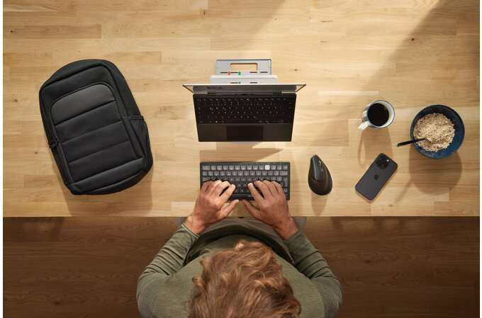 Felülnézet egy asztalról laptop, billentyűzet, egér, kávé és egy fekete hátizsák.