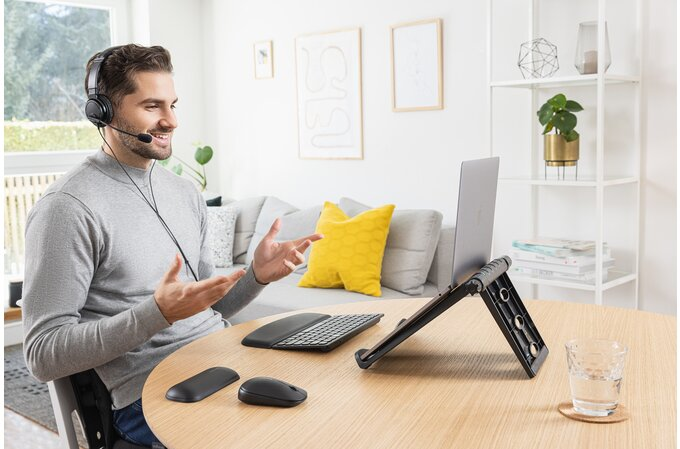 Egy férfi fejhallgatóval laptopot használ, egérrel és billentyűzettel az asztalon.