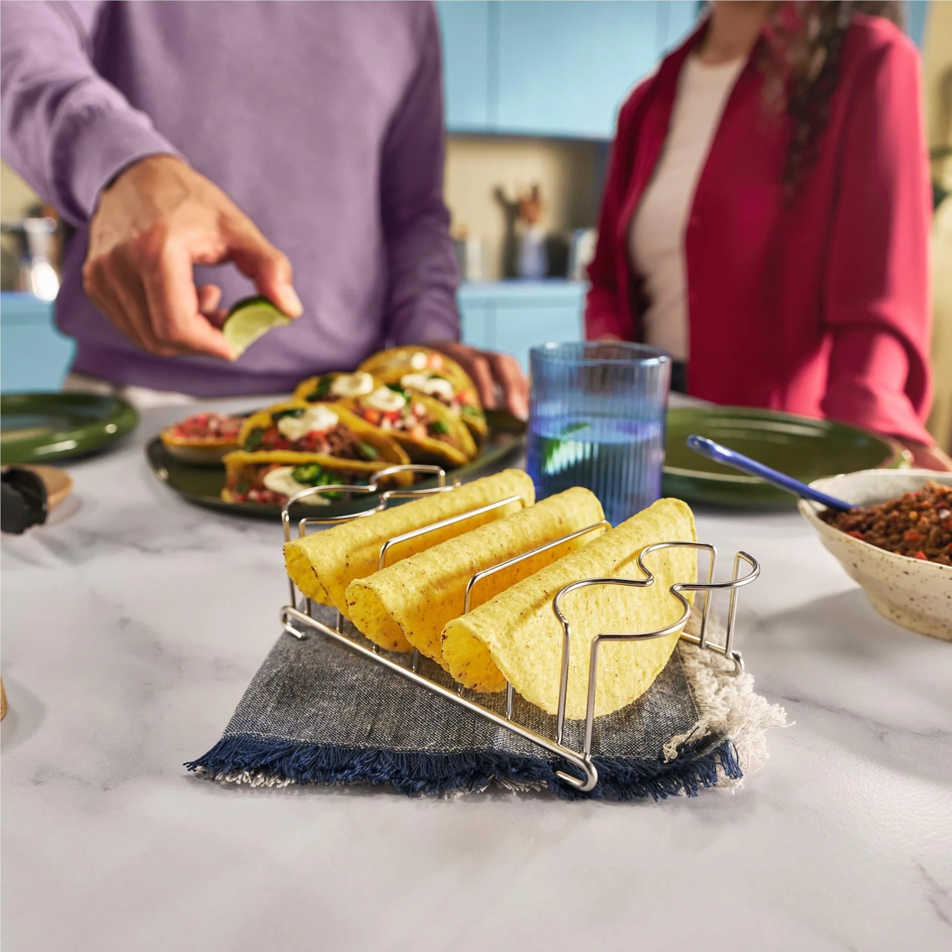 Tacosy w uchwycie, z osobą dodającą limonkę i innymi produktami spożywczymi.