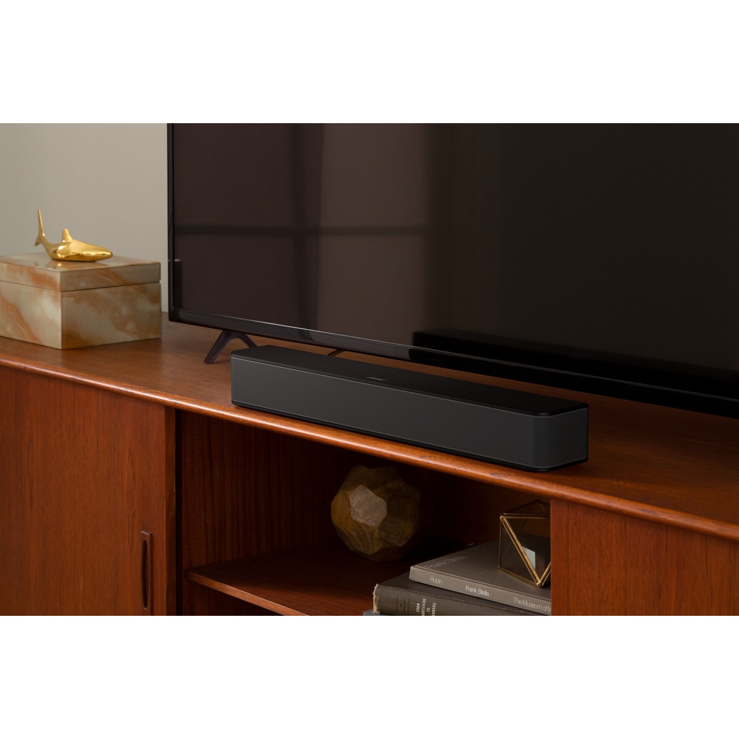 Soundbar su mobile in legno, davanti alla TV. Oggetti: squalo dorato, libri.