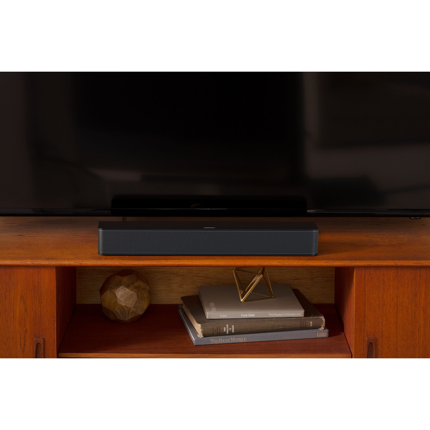 Una soundbar nera poggia su un mobile in legno sotto un grande schermo televisivo nero.