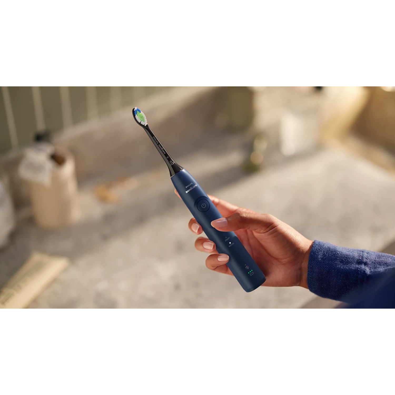 Une main tient une brosse à dents électrique bleu foncé sur un fond clair. La brosse est allumée.